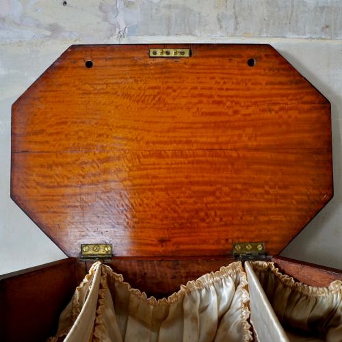 fig 6. An octagonal George III satinwood work table with two drawers, lion mask ring handles, and tapered legs ending in brass castors.