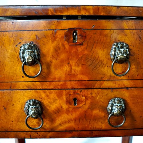 fig 7. An octagonal George III satinwood work table with two drawers, lion mask ring handles, and tapered legs ending in brass castors.