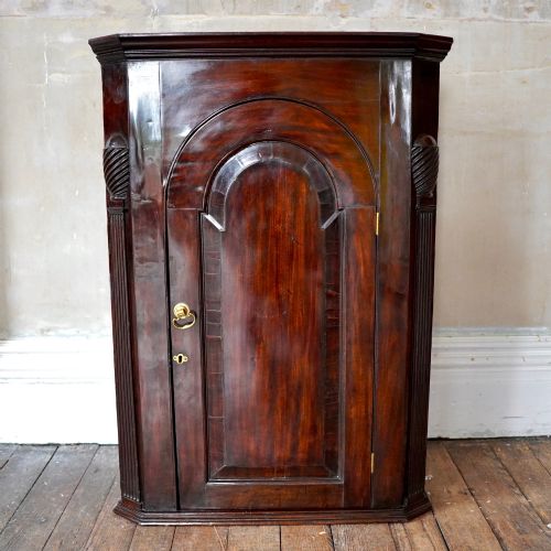 fig 2. Mid-18th century Georgian mahogany hanging corner cupboard featuring an arched panelled door, brass hardware, and fluted pilasters.