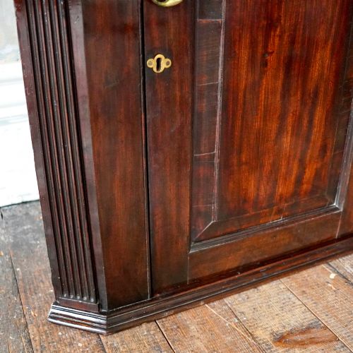 fig 5. Mid-18th century Georgian mahogany hanging corner cupboard featuring an arched panelled door, brass hardware, and fluted pilasters.