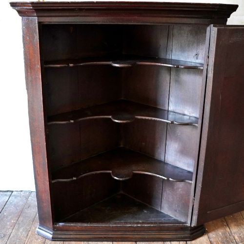 fig 4. A dark oak George III wall-hanging corner cupboard featuring an arched fielded panel door, moulded cornice, and brass escutcheon.