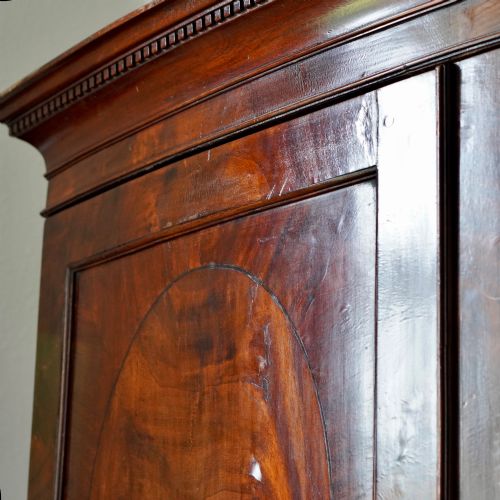 fig 2. A George III bowfront mahogany wardrobe featuring twin panelled doors with oval flame mahogany veneers above two drawers and flared bracket feet.