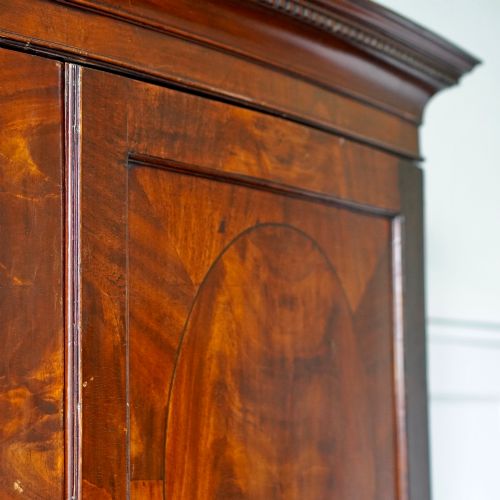 fig 3. A George III bowfront mahogany wardrobe featuring twin panelled doors with oval flame mahogany veneers above two drawers and flared bracket feet.