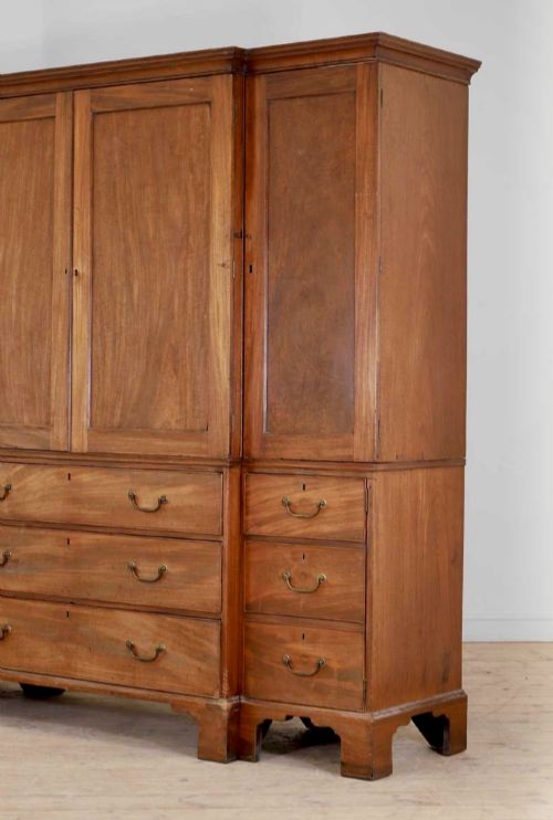 fig 1. A large George III mahogany breakfront linen press wardrobe featuring central panelled doors above drawers, flanked by side cupboards on bracket feet.