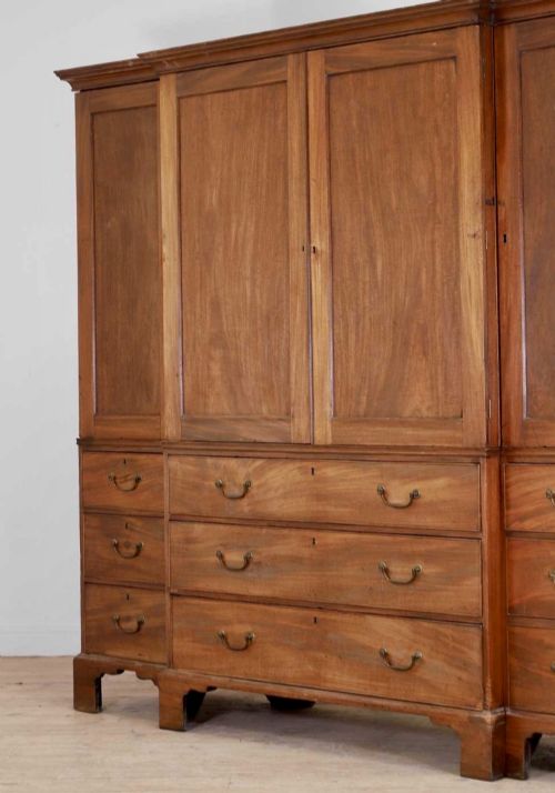 fig 2. A large George III mahogany breakfront linen press wardrobe featuring central panelled doors above drawers, flanked by side cupboards on bracket feet.