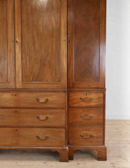 fig 3. A large George III mahogany breakfront linen press wardrobe featuring central panelled doors above drawers, flanked by side cupboards on bracket feet.