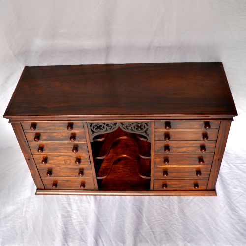 fig 3. A Regency period dark rosewood tabletop collectors cabinet featuring twin banks of small drawers flanking a central mirrored shelf unit with Gothic arched carving.