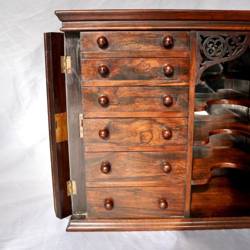 fig 7. A Regency period dark rosewood tabletop collectors cabinet featuring twin banks of small drawers flanking a central mirrored shelf unit with Gothic arched carving.