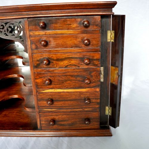 fig 3. A Regency period dark rosewood tabletop collectors cabinet featuring twin banks of small drawers flanking a central mirrored shelf unit with Gothic arched carving.