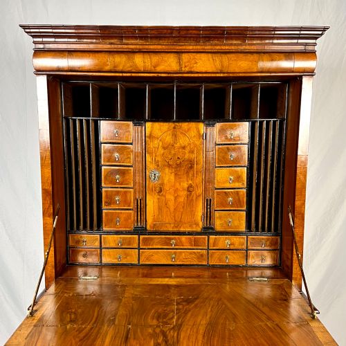 fig 1. An eighteenth-century early Georgian figured walnut escritoire featuring an open fall-front revealing a detailed fitted interior above a lower chest of drawers with brass handles.