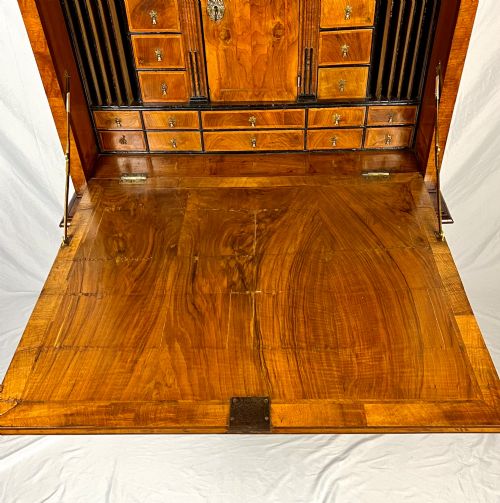 fig 3. An eighteenth-century early Georgian figured walnut escritoire featuring an open fall-front revealing a detailed fitted interior above a lower chest of drawers with brass handles.