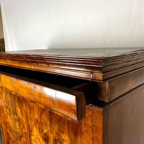 fig 4. An eighteenth-century early Georgian figured walnut escritoire featuring an open fall-front revealing a detailed fitted interior above a lower chest of drawers with brass handles.