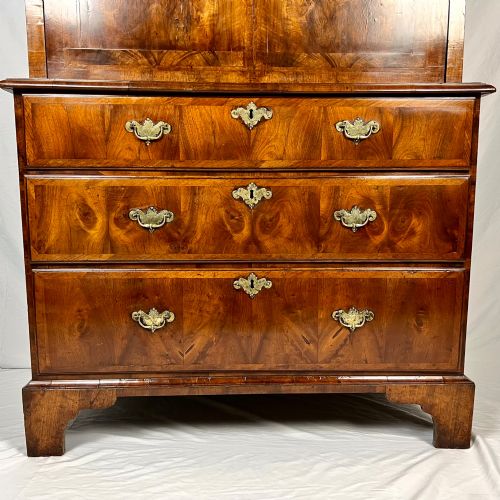 fig 5. An eighteenth-century early Georgian figured walnut escritoire featuring an open fall-front revealing a detailed fitted interior above a lower chest of drawers with brass handles.