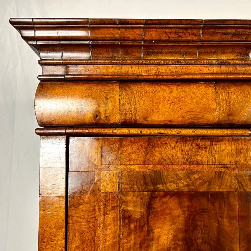 fig 6. An eighteenth-century early Georgian figured walnut escritoire featuring an open fall-front revealing a detailed fitted interior above a lower chest of drawers with brass handles.