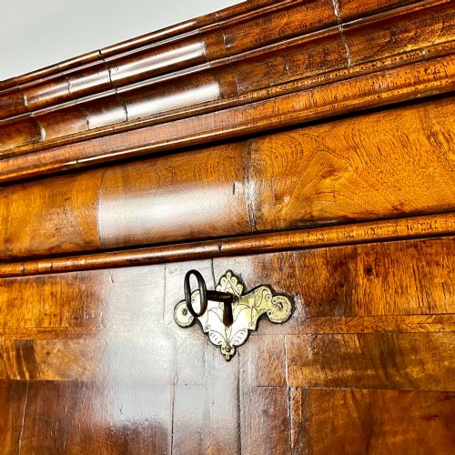 fig 7. An eighteenth-century early Georgian figured walnut escritoire featuring an open fall-front revealing a detailed fitted interior above a lower chest of drawers with brass handles.