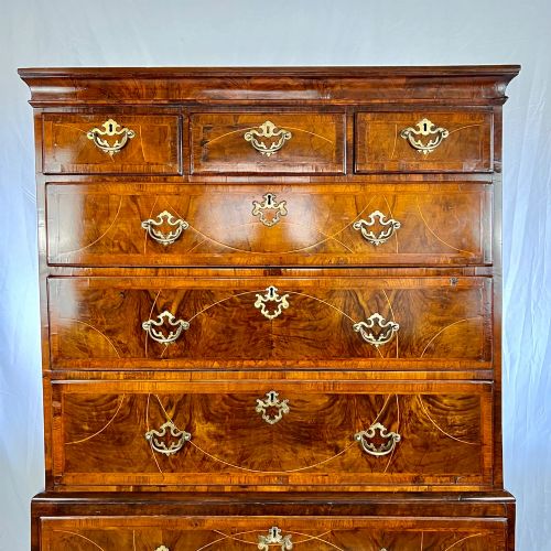 fig 1. A tall George II two-part walnut chest on chest featuring figured burr walnut drawer fronts with line inlay, brass swan-neck handles, and bracket feet.