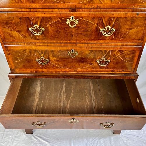 fig 3. A tall George II two-part walnut chest on chest featuring figured burr walnut drawer fronts with line inlay, brass swan-neck handles, and bracket feet.