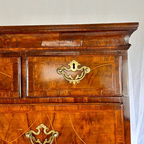 fig 4. A tall George II two-part walnut chest on chest featuring figured burr walnut drawer fronts with line inlay, brass swan-neck handles, and bracket feet.