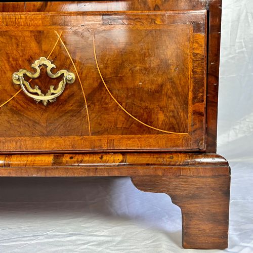 fig 6. A tall George II two-part walnut chest on chest featuring figured burr walnut drawer fronts with line inlay, brass swan-neck handles, and bracket feet.