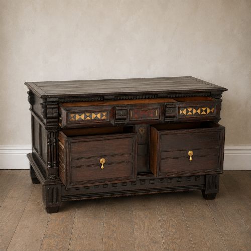 fig 1. A dark oak 17th-century style chest of drawers featuring geometric timber inlay along the top frieze, applied mouldings, and brass drop handles.