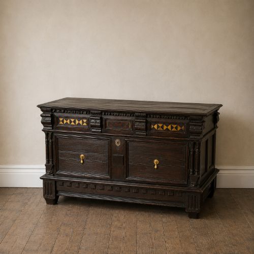 fig 2. A dark oak 17th-century style chest of drawers featuring geometric timber inlay along the top frieze, applied mouldings, and brass drop handles.