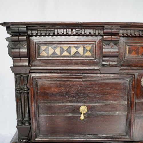 fig 7. A dark oak 17th-century style chest of drawers featuring geometric timber inlay along the top frieze, applied mouldings, and brass drop handles.