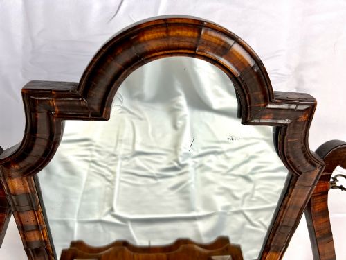 fig 4. An antique Queen Anne walnut and laburnum toilet mirror featuring an arched cross-banded frame above a serpentine base with miniature drawers.