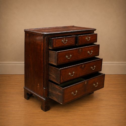 fig 2. A Georgian dark oak chest of drawers featuring two short drawers over three long drawers with mahogany crossbanding and brass swan-neck handles.