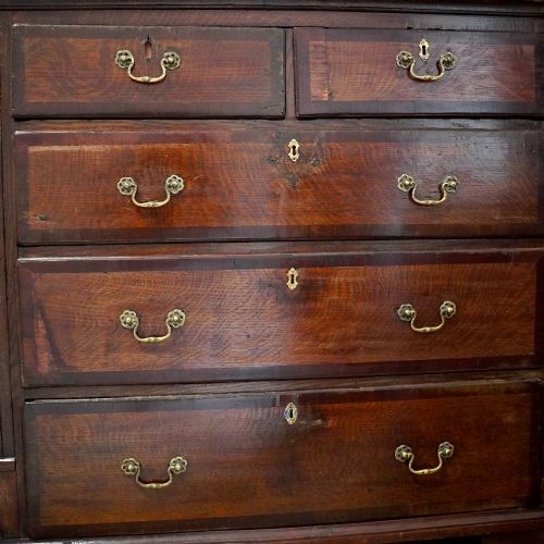 fig 5. A Georgian dark oak chest of drawers featuring two short drawers over three long drawers with mahogany crossbanding and brass swan-neck handles.