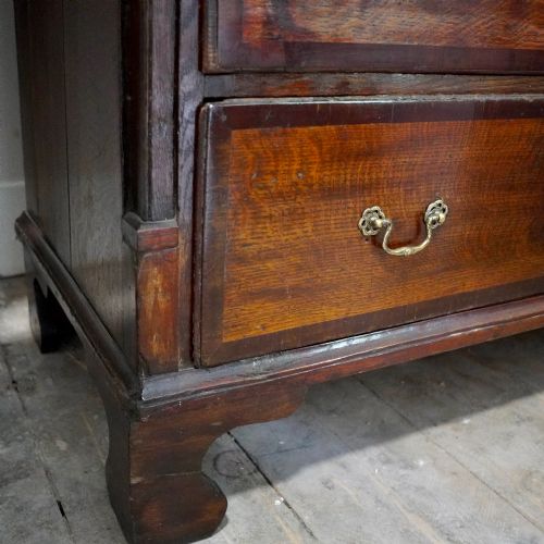 fig 7. A Georgian dark oak chest of drawers featuring two short drawers over three long drawers with mahogany crossbanding and brass swan-neck handles.