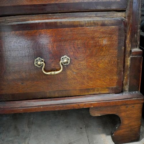 fig 8. A Georgian dark oak chest of drawers featuring two short drawers over three long drawers with mahogany crossbanding and brass swan-neck handles.