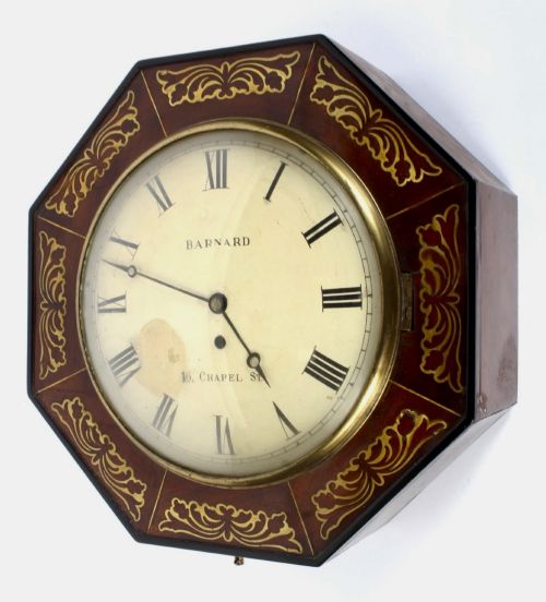fig 2. An octagonal Regency period wall clock in dark mahogany wood with intricate brass foliate inlay and a white dial featuring Roman numerals.