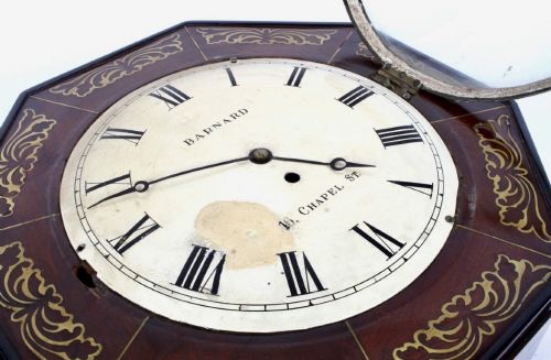 fig 3. An octagonal Regency period wall clock in dark mahogany wood with intricate brass foliate inlay and a white dial featuring Roman numerals.