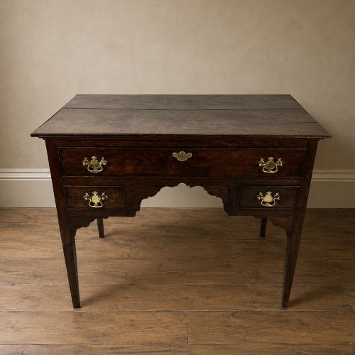 fig 2. An 18th-century Georgian dark oak lowboy side table featuring three drawers with brass handles, a shaped apron, and slender square legs.