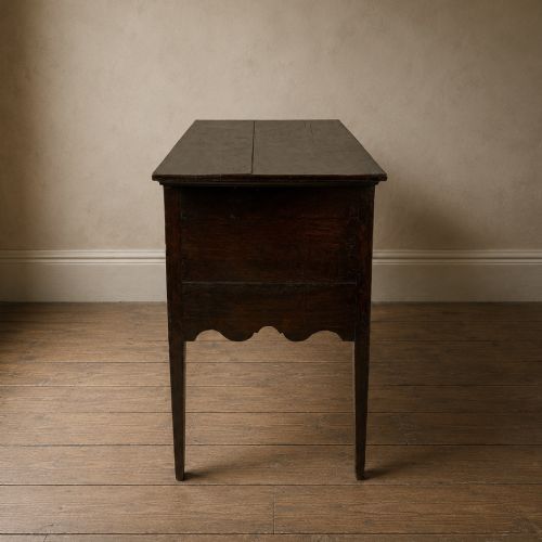 fig 4. An 18th-century Georgian dark oak lowboy side table featuring three drawers with brass handles, a shaped apron, and slender square legs.