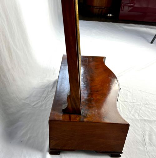 fig 1. A George III mahogany toilet dressing mirror featuring an upright rectangular swing mirror flanked by brass finials, mounted on a serpentine-front base with three small drawers.