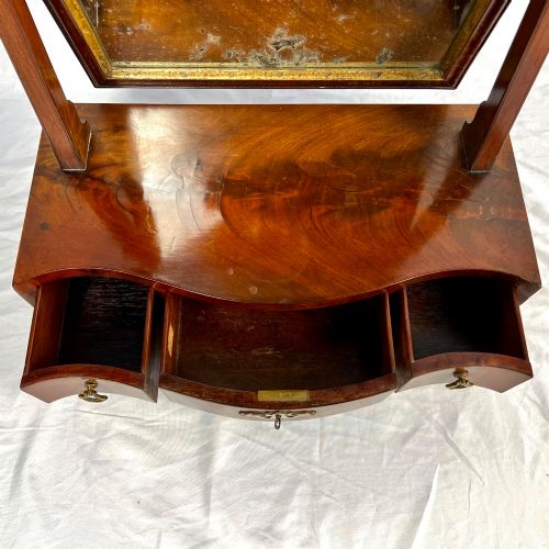 fig 6. A George III mahogany toilet dressing mirror featuring an upright rectangular swing mirror flanked by brass finials, mounted on a serpentine-front base with three small drawers.