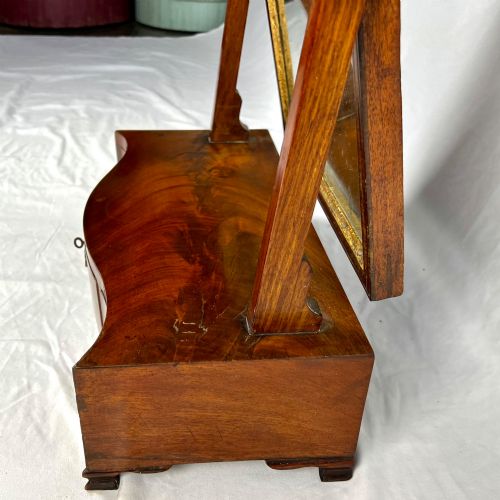 fig 7. A George III mahogany toilet dressing mirror featuring an upright rectangular swing mirror flanked by brass finials, mounted on a serpentine-front base with three small drawers.
