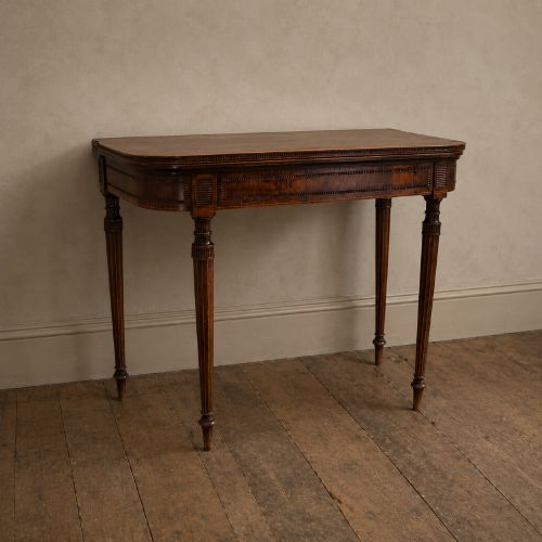 fig 4. An antique Regency rosewood fold-over card table featuring burr yew crossbanding, a rectangular top with rounded corners, and slender fluted tapered legs.