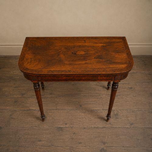fig 6. An antique Regency rosewood fold-over card table featuring burr yew crossbanding, a rectangular top with rounded corners, and slender fluted tapered legs.