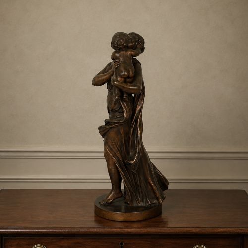fig 7. A patinated dark bronze sculpture depicting a draped classical woman holding a small child against her face, set upon a rounded bronze base.
