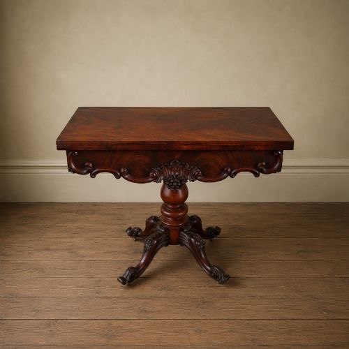 fig 6. A Victorian figured mahogany card table featuring a turnover top, carved frieze, turned pedestal, and scroll legs with castors.