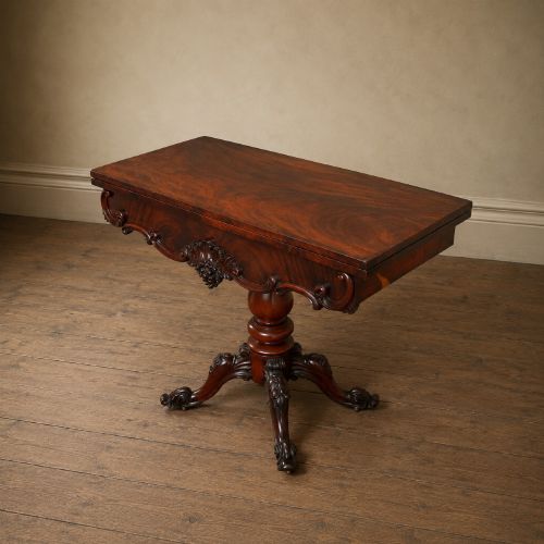 fig 7. A Victorian figured mahogany card table featuring a turnover top, carved frieze, turned pedestal, and scroll legs with castors.
