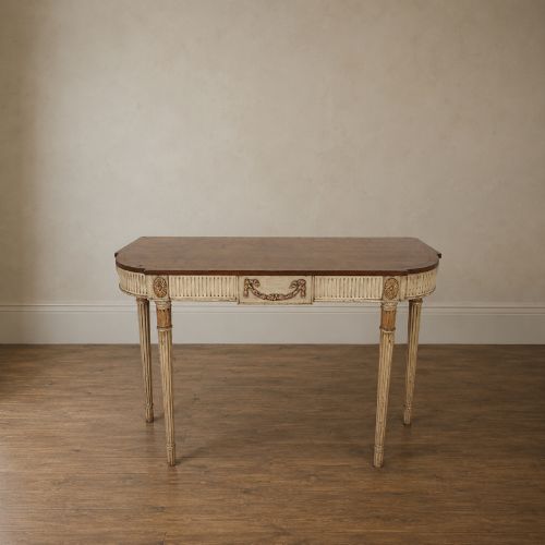 fig 1. A Georgian style painted cream and gilt console table featuring a dark wood top, fluted legs, and carved swag detailing.