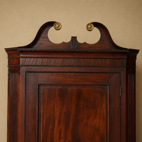 fig 3. A Georgian dark mahogany hanging corner cupboard featuring a swan-neck pediment with brass paterae and a single panelled door with a brass escutcheon.