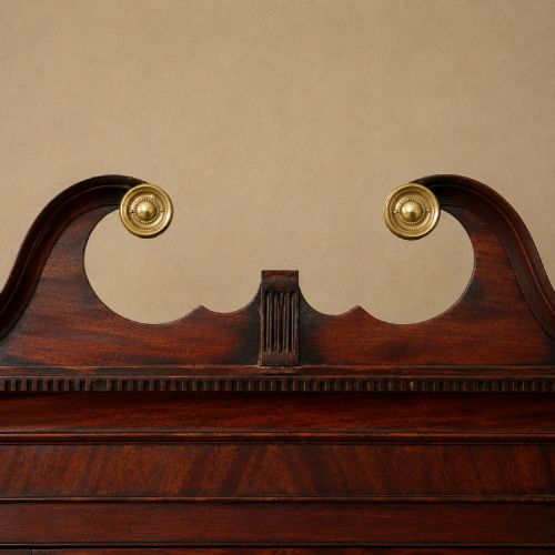 fig 4. A Georgian dark mahogany hanging corner cupboard featuring a swan-neck pediment with brass paterae and a single panelled door with a brass escutcheon.