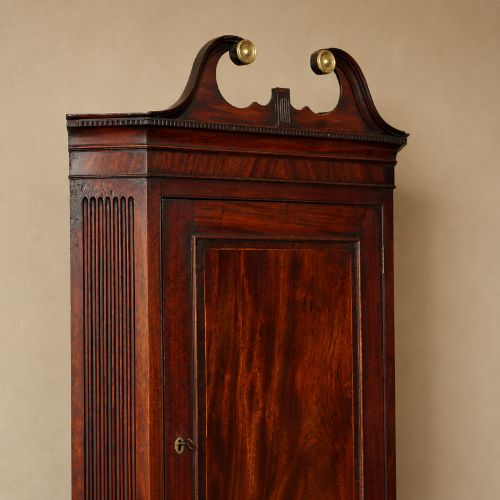 fig 5. A Georgian dark mahogany hanging corner cupboard featuring a swan-neck pediment with brass paterae and a single panelled door with a brass escutcheon.