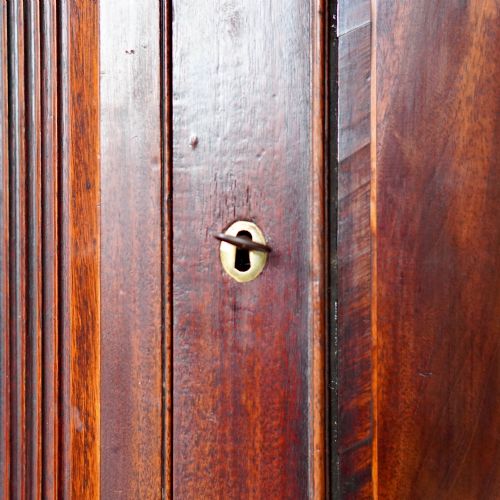 fig 8. A Georgian dark mahogany hanging corner cupboard featuring a swan-neck pediment with brass paterae and a single panelled door with a brass escutcheon.