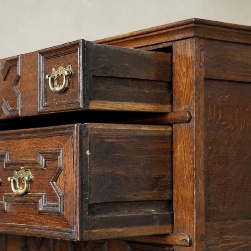 fig 7. An early eighteenth-century oak chest of drawers featuring four drawers decorated with geometric applied mouldings and brass drop handles.