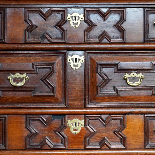 fig 8. An early eighteenth-century oak chest of drawers featuring four drawers decorated with geometric applied mouldings and brass drop handles.